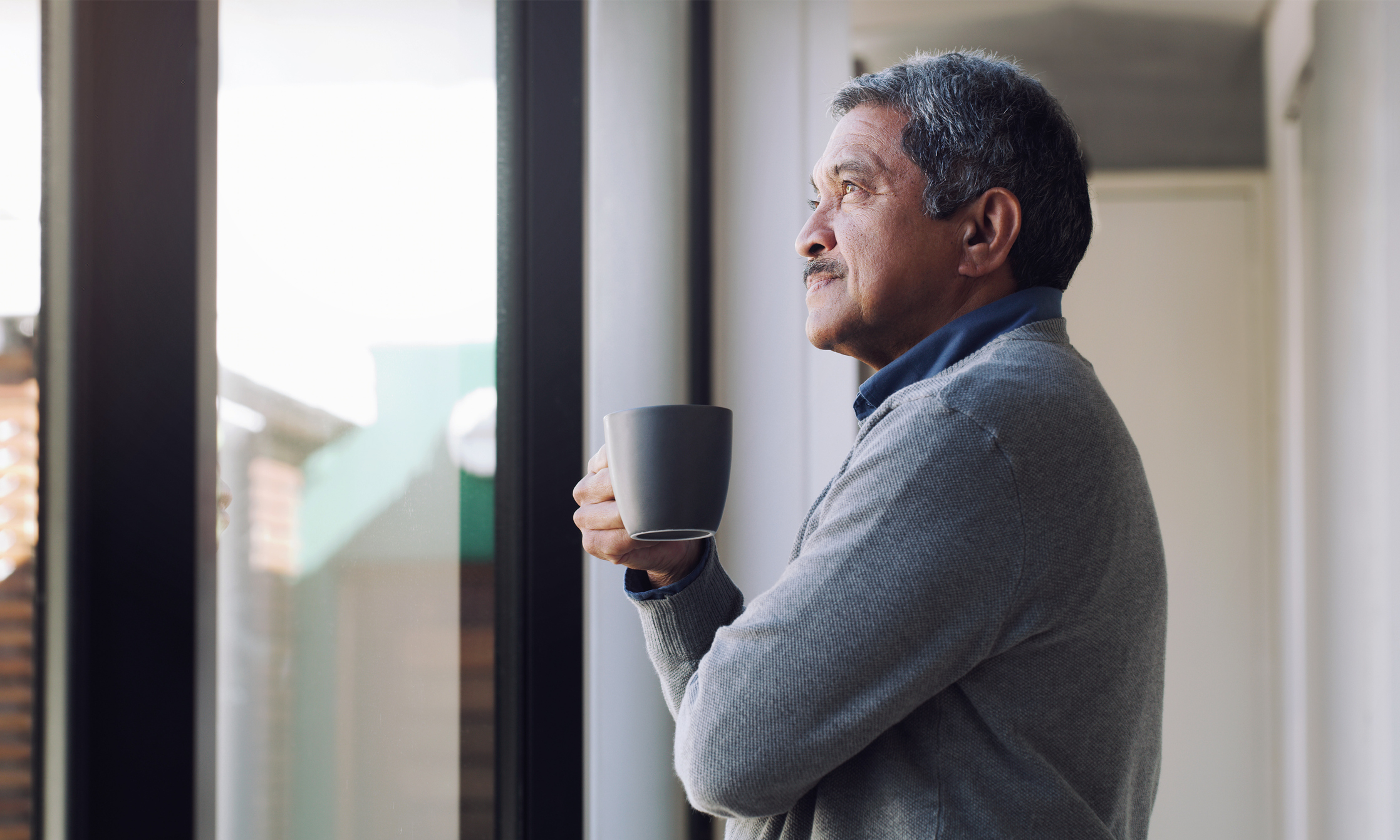Older man looking out the window and holding a mug